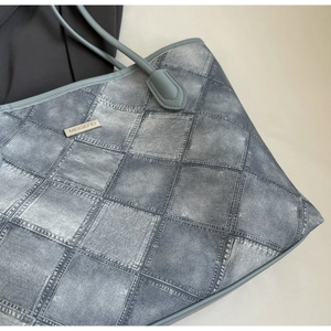 Close-up of vintage tote bag featuring denim patchwork print and metal brand plaque