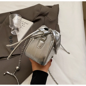 Gros plan du sac seau argenté métallisé avec textures verticales et bandoulière chaîne