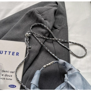 Detail of light blue denim handbag with knotted leather handle and chain strap on grey blazer