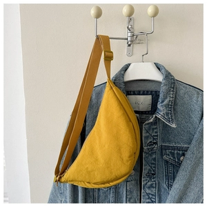 Close-up of yellow nylon dumpling bag with pleated texture and wide strap on denim jacket