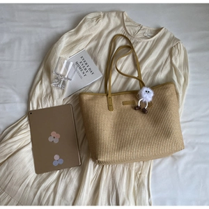 Détail du sac en paille montrant le tissage beige et la bandoulière en cuir avec pompon