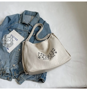 Detail of hobo bag with cream canvas and leather trim on a cozy white sheet backdrop