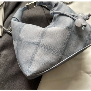 Detailed view of light blue denim dumpling bag featuring quilted diamond pattern and drawstring