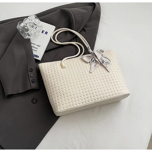 Off-white woven tote bag with silk scarf accessory placed on a dark grey blazer