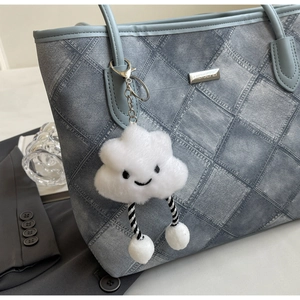 Detail of white plush cloud keychain with smile embroidery on a denim blue tote bag