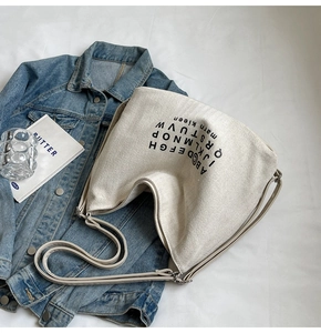 Detail of off-white canvas hobo bag with black letter print on casual denim background