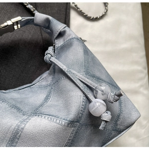 Detail of light blue denim bag with crosshatch pattern and marble bead charm