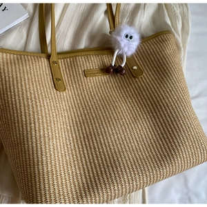 Détail d'un cabas en paille avec bordure en cuir jaune et breloque en peluche