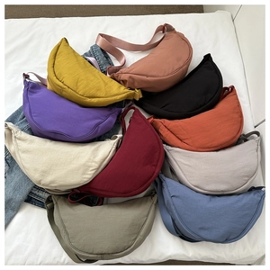 Flat lay of multiple solid colored nylon dumpling bags with adjustable crossbody straps