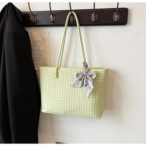 Close-up of light green woven tote bag with decorative silk ribbon on a wooden hook