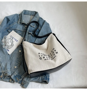 Detail of herringbone canvas hobo bag with black leather trim on white fabric