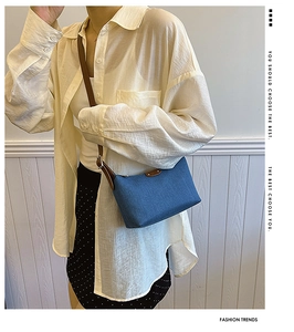 Close-up of vintage blue denim shoulder bag with brown leather strap worn by a model