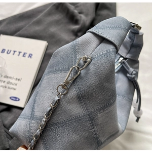 Detail of light blue checkered denim bag featuring silver woven chain and zip closure