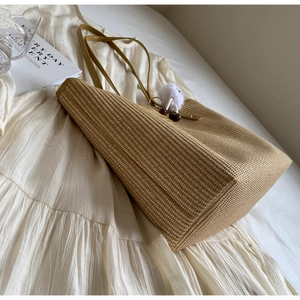 Détail d'un grand sac cabas en paille avec bandoulières en similicuir jaune et pompon blanc