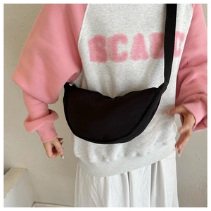 Detail view of a black crescent dumpling bag with adjustable strap on a model outfit
