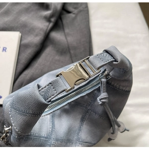 Close-up of light blue denim dumpling bag with metal buckle and checkered dye pattern