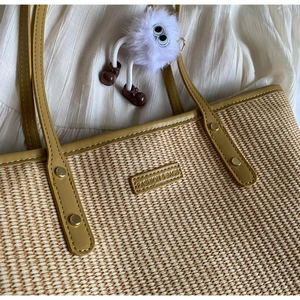 Détail du sac cabas en paille avec garniture en similicuir jaune et grigri peluche