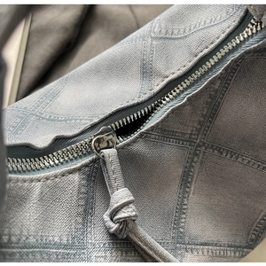 Detailed macro view of high-quality silver metal zipper with woven knot pull on blue textured bag