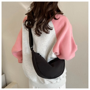 Detail of a black crescent nylon crossbody bag worn over a pink and grey hoodie