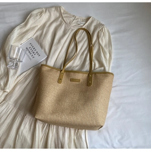 Détail d'un sac cabas en paille d'été avec anses en cuir PU jaune moutarde sur un lit