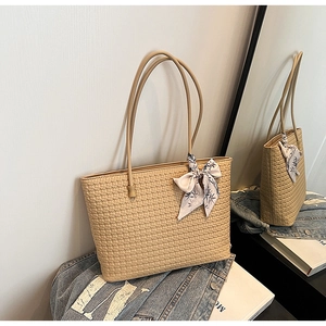 Detail of beige woven tote bag with silk scarf bow accent and long shoulder straps