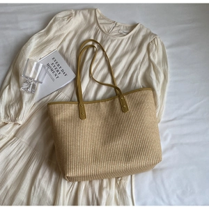 Détail d'un cabas en paille beige avec anses en cuir jaune moutarde et rivets dorés