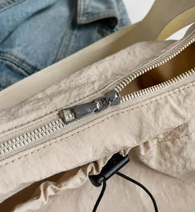 Close-up of smooth silver metal zipper and pleated fabric on a beige crossbody bag