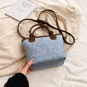 Detailed close-up of light blue denim bucket bag featuring delicate white flower embroidery