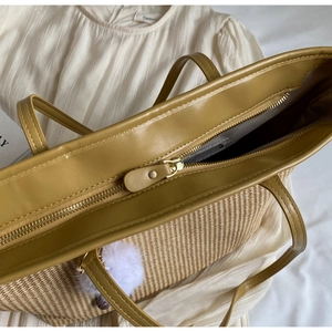 Détail d'un sac cabas en paille tressée avec bordure en cuir, fermeture éclair et pompon