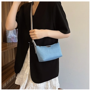 Close-up of a light blue denim mini crossbody bag with a sleek metal logo plate