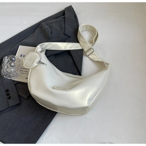 Detail of a creamy white half-moon hobo bag with a round coin pouch and leather logo tag