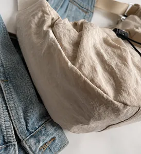 Detail of beige pleated nylon shoulder bag with drawstring buckle on denim background