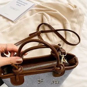 Detail view of denim bucket bag showing brown leather handles and adjustable shoulder strap
