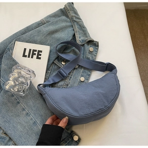 Close-up of a blue nylon half-moon hobo bag styled on a denim jacket with lifestyle props