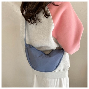 Rear view of a model wearing a blue nylon crescent dumpling bag with pleats and zipper