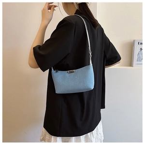 Side view of woman wearing a light blue denim underarm bag with silver strap and metal logo