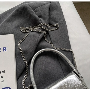 Detailed top view of a silver metallic chain bag on gray fabric and white book