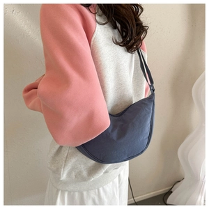 Blue crescent dumpling bag with thick woven strap shown from a stylish side perspective