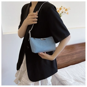 Detail of light blue denim crescent underarm bag with silver zipper and metallic logo