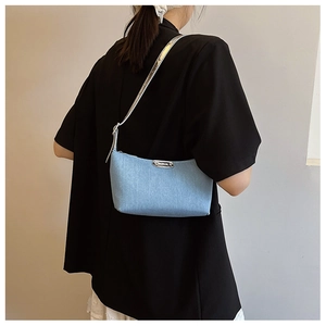 Detail of light blue denim shoulder bag featuring silver metal plaque and chain strap