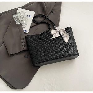 Detail of black woven tote bag featuring a floral silk scarf bow and slim shoulder strap