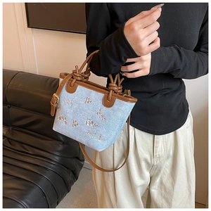 Detail of blue denim bucket bag with white floral embroidery and brown knotted handle