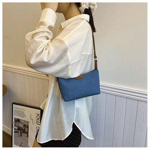 Model view of a vintage denim blue shoulder bag with brown leather straps and zip closure