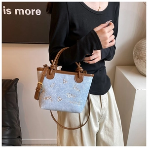 Detail of light blue denim bucket bag featuring white floral embroidery and brown leather handle