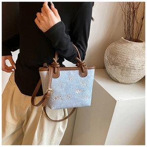 Close-up of denim canvas bucket bag with floral embroidery and brown knotted handle