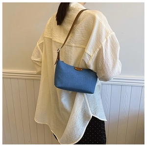 Detail of vintage denim baguette bag with brown leather strap worn by a model
