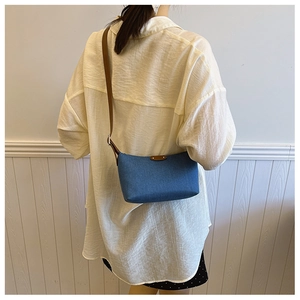 Detail of retro blue denim crescent shoulder bag with brown leather strap and trim