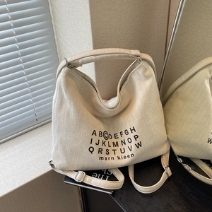 Large beige canvas tote bag with black alphabet print and shoulder strap in natural light
