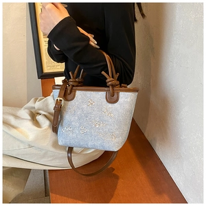 Detail of light blue denim bucket bag with floral embroidery and brown leather straps
