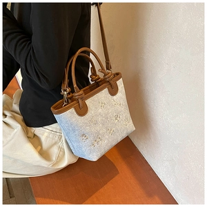 Detail view of denim canvas bucket bag with white embroidery and brown leather trim